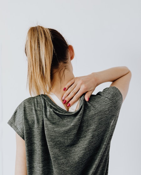 Young woman rubs back of neck.