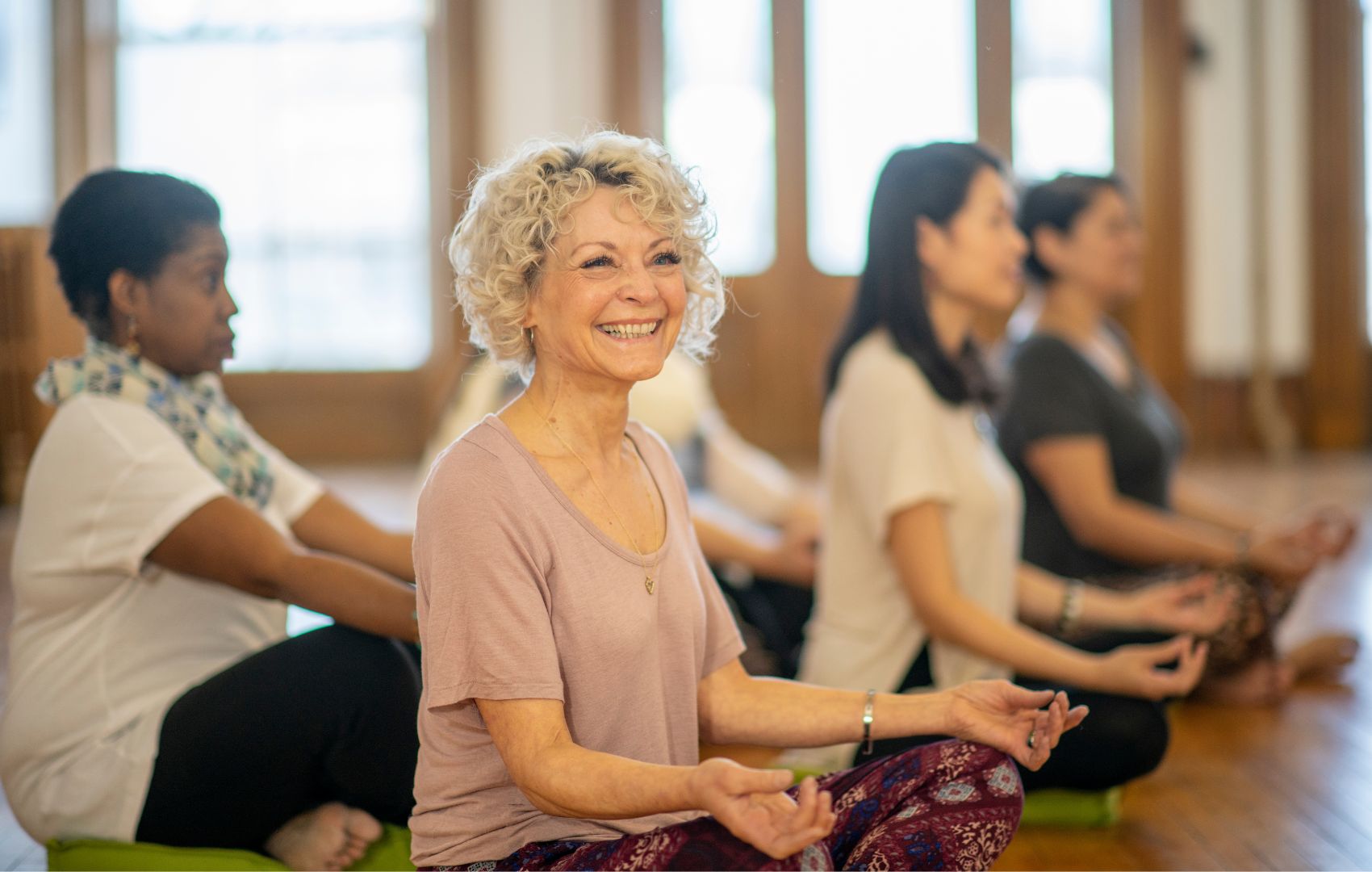 Diverse group of yoga practitioners sitting on floor. At forefront is older woman, smiling.